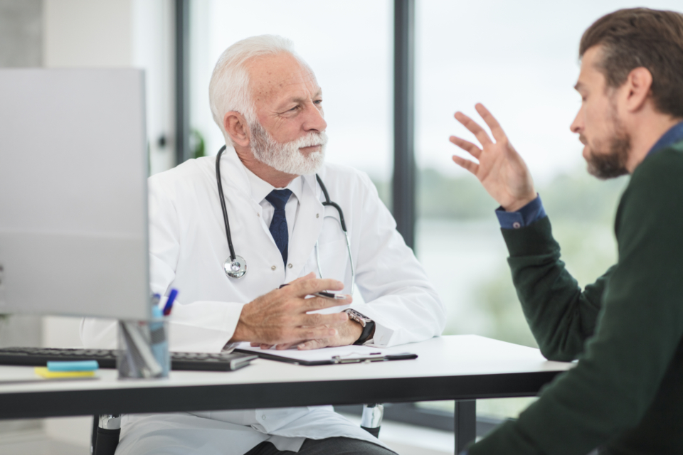 Doctor talking with a patient next to a computer, showing how doctors use AI during appointments